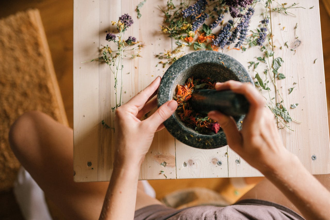 services-03 Hands using a mortar and pestle to grind colorful dried herbs on a wooden table.