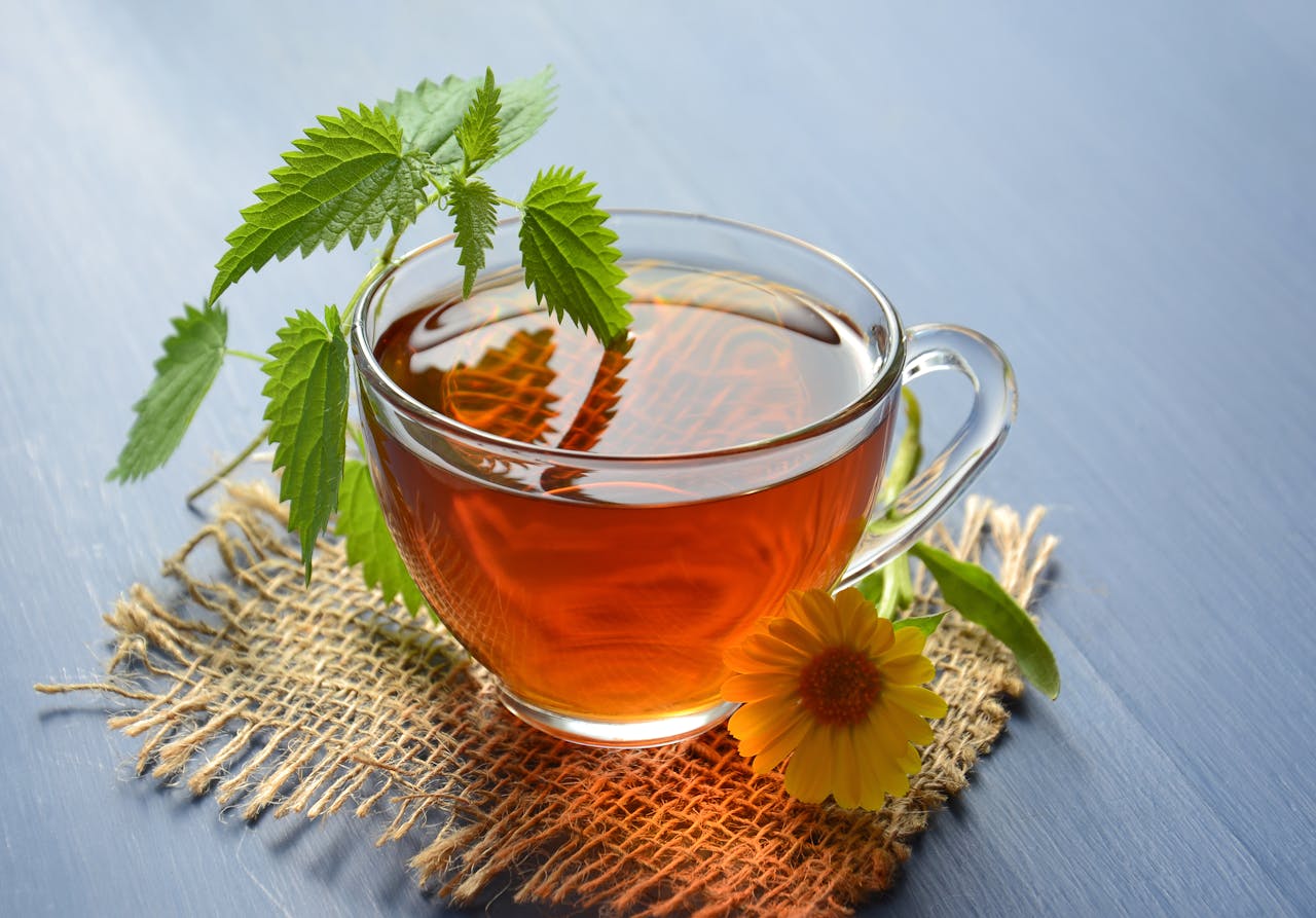 about-02 A refreshing glass cup of herbal tea garnished with nettle leaves and marigold flower.